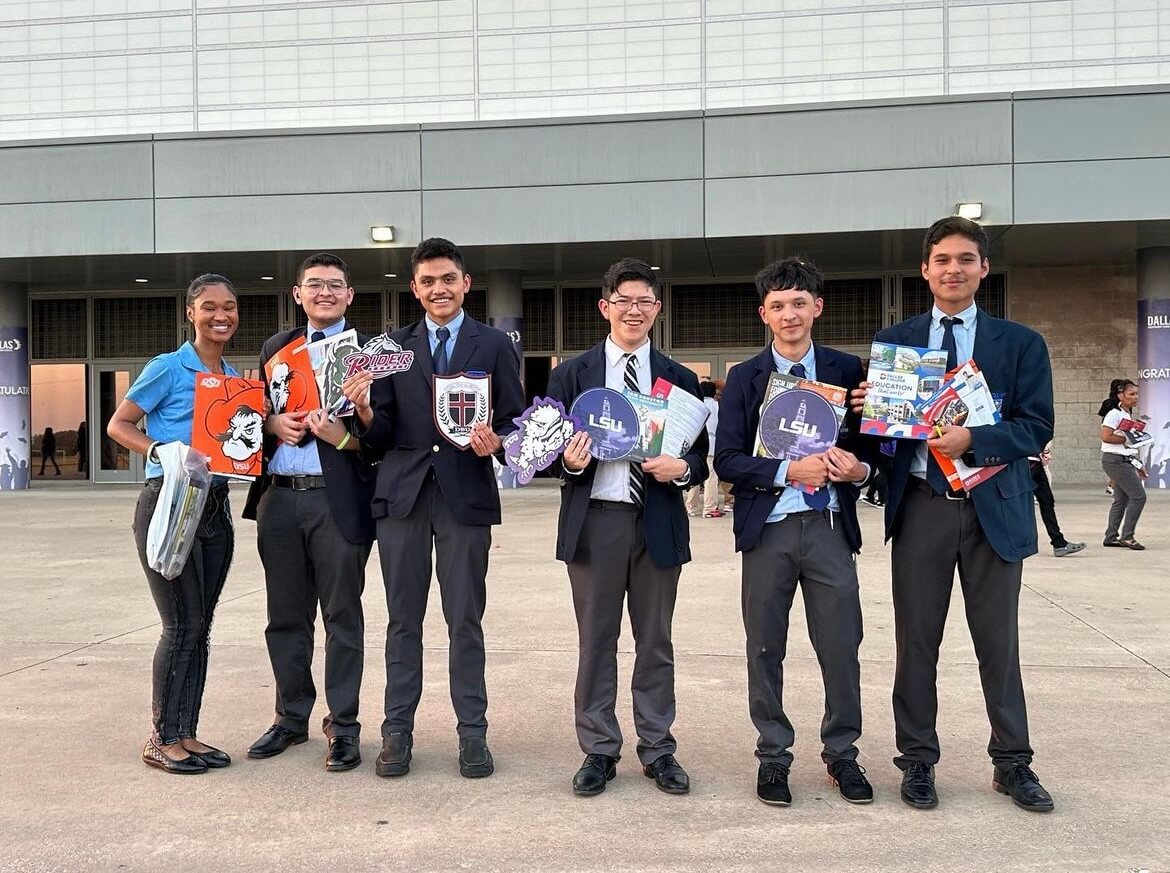 Students pose in front of a building holding college materials