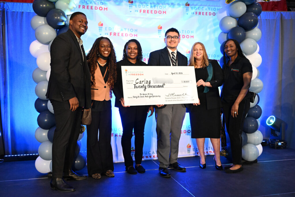 First 20k Lacy Scholarship recipient standing with a team of professionals while holding a large, gifted check